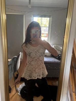 Beige spetsblus med volang - Säljer en söt beige blus i spets med volang nedtill och rund halsringning. Blusen är ärmlös och har ett fint blommigt spetsmönster som ger en romantisk vibe. Perfekt att styla med jeans eller kjol för en trendig look.