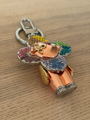 Vuitton Nyckelring apa med regnbågskristaller - Säljer en unik nyckelring i form av en apa dekorerad med glittrande kristaller i regnbågens färger. Kroppen är i roséguldigt metallmaterial och öronen samt kroppen är täckta av färgglada stenar. Perfekt som accessoar till väskan eller nycklarna.