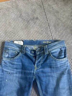 Blå raka jeans från DonDup  - Blå jeans från Stan D'art med raka ben och slitningar. Jeansen har kontrastsömmar i gult, klassisk femficksmodell och knappgylf. Perfekt för en avslappnad och trendig stil. W28 