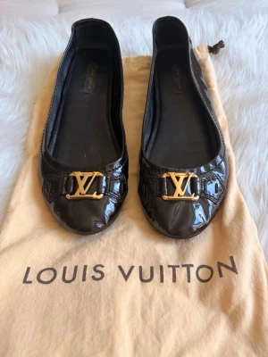 Louis Vuitton Dreamy Rose ballerinaskor - Louis Vuitton Dreamy Rose ballerinaskor i svart lackläder med guldfärgat LV-spänne.  Skick: Begagnade i fint skick med normalt bruksslitage. Köpta via Vestiaire Collective.  * Fint skick på lacklädret med naturliga veck efter användning. * Guldfärgade LV-spännen i fint skick. * Sulorna har gott om mönster kvar. * Normalt slitage på innersulorna. * Se samtliga bilder för en rättvis bedömning. 