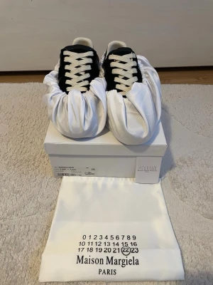 Maison Margiela GATs/ strl 42 svart&gummi - Maison Margiela sneakers i svart mocka och läder med vita kontrasterande skosnören och gummisula. Klassisk low-top silhuett och stilren design. Kommer med originalpåse och box. Perfekta för dig som gillar minimalistisk och exklusiv stil. Priset ej hugget i sten! Fraktas om 24h