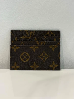 Brun monogram korthållare - Snygg korthållare   i klassiskt brunt monogrammönster. Tillverkad i tåligt läder med flera fack för kort. Perfekt för dig som vill ha en stilren och lyxig accessoar i fickan.