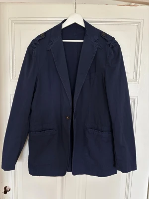 Etro Milano mörkblå kavaj  - Stilren mörkblå kavaj från Etro Milano med klassisk passform, två framfickor och en bröstficka. Kavajen har snygga axeldetaljer med knappar och är tillverkad i ett lätt tyg som passar perfekt till en dressad look.
