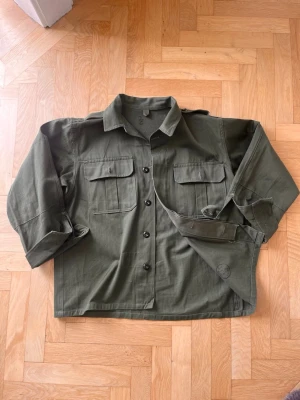 Mörkgrön militär jacka - Olivgrön militärjacka, köptes på Broadway and sons, stolen s/m passar bra på ca 178 +- 2 cm lång person, skjortan har lite lösa sömmar osv. Men det var så när jag köpte så det ger bara vintage look 