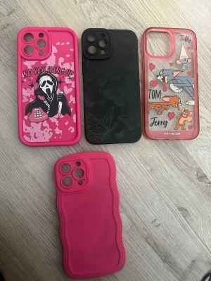Fyra färgglada mobilskal med motiv - Säljer fyra olika mobilskal för smartphone. Ett rosa med Scream-motiv och text, ett svart med fjärilsmönster, ett transparent med Tom & Jerry-tryck och ett enfärgat rosa med vågig kant. Skalen är gjorda i plast eller silikon och har olika kreativa designer. 100kr för alla. iPhone 13 Pro Max 