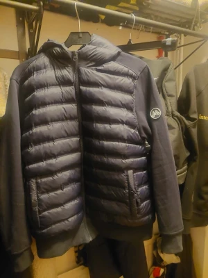  Maggiore cardigan HELT NY - Snygg mörkblå pufferjacka från Maggiore med quiltad front och huva. Jackan har mjuka ärmar och sidor i sweatshirtmaterial, två fickor med dragkedja och en logga på ärmen. Perfekt för kalla dagar och riktigt skön att bära.  Den är helt ny  säljer den pågrund av att jag valt fel storlek
