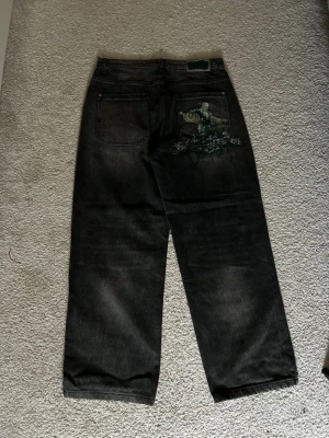 (Derschutze)Svarta raka jeans med tryck - Säljer ett par svarta jeans med baggy passform och christ the redeemer på bakfickan. Jeansen har en avslappnad look, perfekta för dig som gillar streetwear och vill sticka ut lite extra.