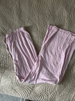 Ljusrosa mjuka loungewear-byxor - Superbekväma loungewear-byxor i ljusrosa färg med resår och dragsko i midjan. Tillverkade i ett mjukt och tunt material som känns skönt mot huden. Perfekta för att chilla hemma eller mysa i soffan.