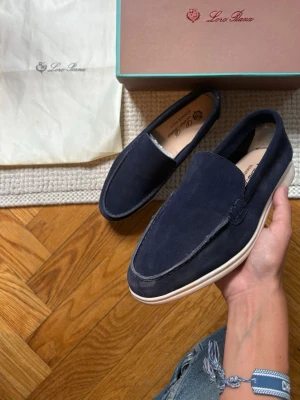 Mörkblå mocka loafers Loro Piana - Snygga mörkblå loafers från Loro Piana i mjuk mocka med vit sula. Klassisk slip-on modell med stilren design och diskreta sömmar. Perfekta för dig som gillar en clean och tidlös look.