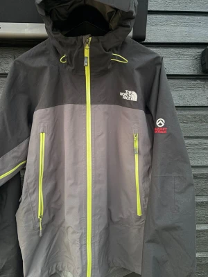 The North Face Summit Series vindjacka - Skaljacka i herrstorlek L/G från The North Face Summit Series, nästintill nyskick och bara använd ett fåtal gånger. Färgkombination i svart och grått, med gröna detaljer. Den är har deras GORE-TEX Pro Shell som ger ett extremt bra skydd med en vattenpelare på minst 28 000 mm och 3-lagerskonstruktion. Alltså den serie som är gjord för extrema alpina förhållanden. Ventilationsdragkedja finns till armhålorna. Inbyggd skärm i huvan med spännen både fram och bak. Ordinare pris: 6000 