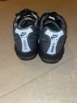 Nike Air svarta sneakers med camo-detaljer - Nike Air sneakers i svart med grå och vita detaljer samt camo-mönstrad insida. Skorna har snörning, reflekterande paneler och unika siffror på hälen. Ovandelen har mesh och syntetmaterial för en sportig look.