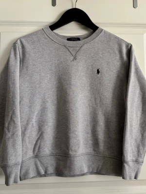 Polo Ralph Lauren grå sweatshirt M 10–12 år  - Polo Ralph Lauren sweatshirt i grått 🤍  Snygg och stilren Polo Ralph Lauren sweatshirt med klassisk broderad logga på bröstet. Tidlös modell som är enkel att matcha och passar perfekt till vardags. ⭐  📏 Storlek: M / 10–12 år 📐 Längd: 53 cm 📐 Bredd: 48 cm ✨ Skick: Mycket bra skick – inga hål, fläckar eller andra skador.  Måtten är tagna när tröjan ligger plant.  💬 Lägg gärna ett bud! Har du frågor eller vill ha fler bilder är det bara att skriva – svarar så snabbt som möjligt. 📩