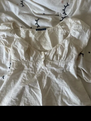 Vit blus med puffärm och knappar - Supersöt vit blus med puffärmar och v-ringning. Blusen har knappar framtill och är sydd i ett lätt bomullstyg som känns luftigt. Perfekt för dig som gillar romantisk och feminin stil.