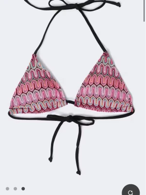 Färgglad randig bikini med knyt - Säljer en snygg trekantsbikini med vågiga ränder i rosa, rött, blå, vitt och svart. Både överdel och underdel har knytband för justerbar passform. Använd endast 3gånger. Perfekt för sommaren och strandhäng!