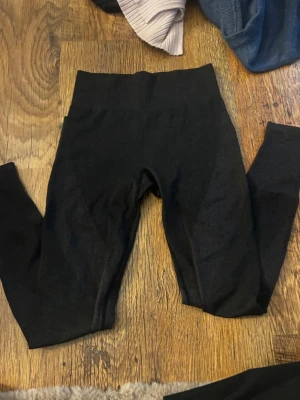 Svarta sömlösa leggings - Säljer ett par svarta sömlösa leggings med hög midja och stretchigt material. De har en ribbad linning och sitter tight längs benen, perfekta för en sportig och bekväm look. Passar till både träning och chill.