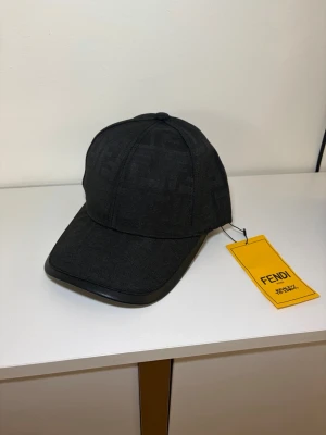 Svart keps från Fendi - Snygg svart keps från Fendi med diskret FF-mönster i tyget och böjd skärm med läderdetalj. Kepsen har klassisk sexpanelsdesign och justerbar passform. Perfekt accessoar för en trendig look.
