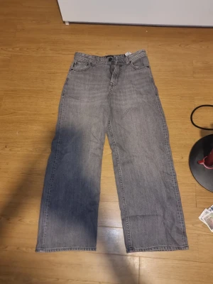 Gråa raka baggy jeans från Jack & Jones - INSTABOX!!! Ett par gråa baggy jeans från Jack & Jones med rak passform och hög midja. Klassisk femficksmodell med knapp och dragkedja framtill. Jeansen är tillverkade i denim och har en avslappnad look som passar perfekt till en trendig vardagsstil. Aldrig andvända!