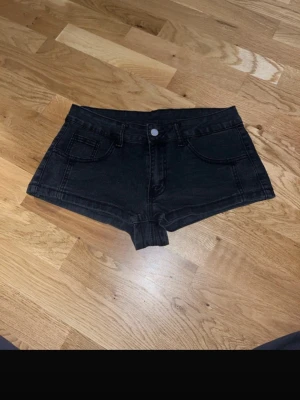 Svarta denimshorts med låg midja - Snygga svarta shorts i denim med låg midja och klassisk femficksdesign. De har knapp och dragkedja framtill samt bälteshällor. Perfekta för varma dagar och enkla att matcha med olika toppar.