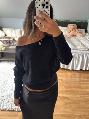 Svart off shoulder tröja - Trendig svart off shoulder tröja från bikbok med avslappnad passform och långa ärmar. Mjuk och bekväm, perfekt att styla med kjol eller jeans. Ribbstickade muddar vid ärmslut och nederkant ger en snygg finish. 