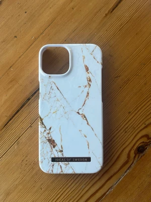 Vitt marmormönstrat mobilskal för iPhone 13 - Snyggt mobilskal från iDeal of Sweden med vitt marmormönster och guldfärgade detaljer. Skalet är gjort i hårdplast och har en stilren design med öppning för kamera. Insidan är klädd i mjukt material för extra skydd.