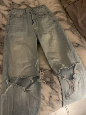 Ljusblå jeans med raka ben - Säljer ett par ljusblå jeans med raka ben och stora hål över knäna. Jeansen har medel hög midja. nypris 599kr, pris kan diskuteras 