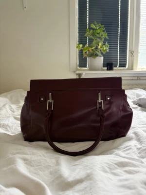 Vinröd handväska - Jättesnygg vintage vinröd handväska från Bershka! Sparsamt använd inget synligt slitage. Rymlig med två större fack och ett innerfack med dragkedja.
