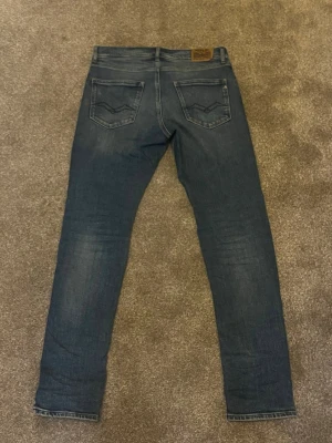 Mörkblå replay slim fit jeans ( 14a/S ) - Säljer ett par mörkblå slim fit jeans med lätt slitna detaljer och klassiska fem fickor. Jeansen har en snygg tvätt och raka ben, perfekta för en avslappnad men stilren look. Materialet är mjukt denim som sitter skönt hela dagen.