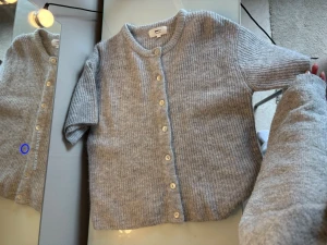 Ljusgrå ribbad kofta med kort ärm - Kortärmad ljusgrå kofta i ribbstickat material med rund halsringning och vita knappar framtill. Perfekt för lager på lager och enkel att styla till olika outfits. Säljer för att jag inte har någon användning för den längre.