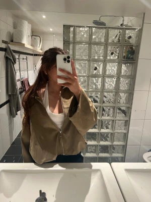 Beige oversized vindjacka med dragkedja - Snygg beige vindjacka i oversized modell med hög krage och dragkedja framtill. Jackan har justerbara band i nederkant och två sidofickor. Perfekt för en chill och trendig look till vardags. Materialet ser ut att vara tunt och smidigt, vilket gör den enkel att bära.