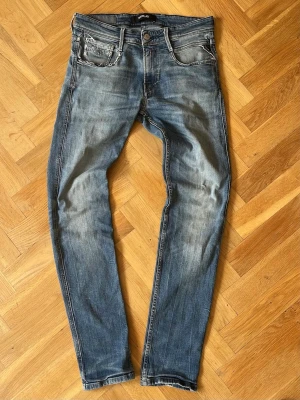 Blå slim fit jeans Replay - Snygga blå slim fit jeans från Replay med slitna detaljer och ljusa tvättade partier. Klassisk femficksmodell med knappgylf och bälteshällor. Jeansen har en modern passform och är tillverkade i denim med lätt stretch för extra komfort.