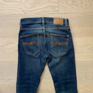 Nudie Jeans Grim tim - Snygga nudie jeans i snygg wash. Skicket är super och modellen heter grim tim. W27/32 KOM MED PRISFÖRSLAG. OBS två medel stora hål i skrevet. Syns 