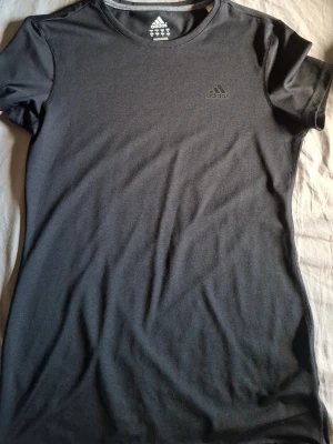 Svart t-shirt från Adidas - Svart t-shirt från Adidas med diskret logga på bröstet. Klassisk rund halsringning och korta ärmar. Tillverkad i mjukt material som passar perfekt till en sportig stil eller till vardags. Enkel och stilren design.
