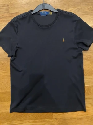 Svart t-shirt från Polo Ralph Lauren - Klassisk svart t-shirt från Polo Ralph Lauren med rund hals och broderad logga på bröstet. Enkel och stilren design som passar till det mesta. Tillverkad i mjuk bomull för skön komfort.