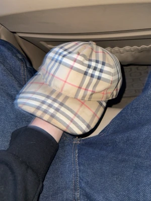 Beige burberry keps  - Snygg beige keps med rutigt mönster i svart, vitt och rött. Kepsen har böjd skärm och justerbar rem bak. Perfekt accessoar för en trendig streetwear-look. Materialet känns mjukt och följsamt, och designen är riktigt tidlös. Använd en gång bara legat hemma sen dess 