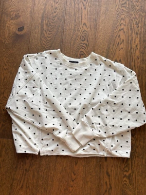 Vit sweatshirt med svarta prickar - Vit sweatshirt från VINYL ICONS med svarta prickar över hela tröjan. Tröjan har rund halsringning, långa ärmar och ribbade muddar vid ärmslut och hals. Perfekt för en avslappnad och trendig stil. Den är avklippt längst ner då den hade en mudd jag inte gillade, men tycker den sitter fint!! Köpt i usa så ingen koll på märket! 