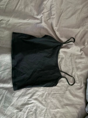 Svart linnetopp från H&M Divided - Enkel och stilren svart linnetopp från H&M Divided med smala axelband. Perfekt att matcha med jeans eller kjol för en clean look. Mjuk och bekväm, passar till många olika outfits.
