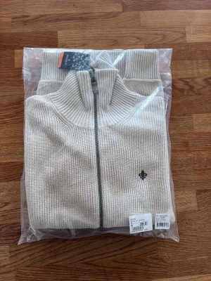 NY Morris Cardigan Beige - Helt ny beige cardigan från Morris, aldrig använd. Stickad modell med hög krage och dragkedja framtill. Klassisk och stilren färg som passar till det mesta.  Nypris: 1 899 kr. Säljes för 999 kr.  Skickas i originalförpackning.