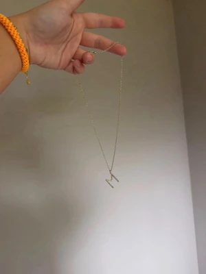 Maria Nilsdotter halsband med bokstaven M - Snyggt halsband i guldfärgad metall med ett hängsmycke i form av bokstaven M. Kedjan är tunn och stilren, perfekt för dig som vill ha en personlig touch på din outfit. Passar lika bra till lager på lager som för sig själv.