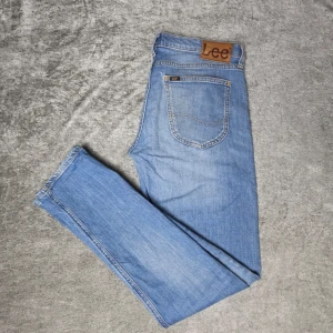 Lee Luke jeans blå W31 L32 - Blå jeans från Lee i modellen Luke. Klassisk femficksmodell i ljusblå tvätt med stretch för en bekvämare passform.  Storlek W31 / L32 Modell Luke  Bra begagnat skick med normalt bruksslitage.  Mindre hål finns höger bakficka, se bilder.  Mått Midja: ca 40 cm Grenhöjd: ca 22 cm Ytterlängd: ca 101 cm Innerbenslängd: ca 78 cm Benöppning: ca 15 cm  Material 99% bomull 1% elastan  Varan är begagnad och säljs i befintligt skick, se bilder för detaljer.
