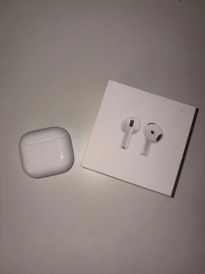 Airpods 4 (2024) - Säljer ett par trådlösa vita hörlurar med laddningsetui. Hörlurarna har stilren design och levereras i originalförpackning. Perfekta för musik, poddar och samtal på språng. Laddningsetuiet är kompakt och lätt att ta med sig.