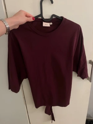 Vinröd topp med knyt i ryggen - Säljer en vinröd topp med halvlånga ärmar och  knytning i ryggen från Nelly💞