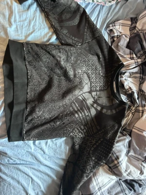 Svart sweatshirt med mönster från Dolce Gabbana -  svart sweatshirt från Dolce Gabbana med unikt mönster i grått och svart, bland annat hjärtan, blommor och geometriska former. Tröjan har ribbade muddar vid ärmslut och nederkant. Perfekt för dig som gillar streetwear och grafiska prints. Köpt på best secret, sitter som M. Använd 1 gång kan gå ner i pris vid snabb affär🙌