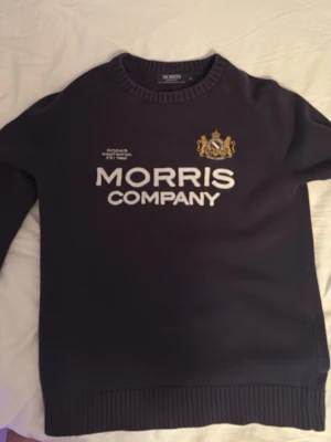 Morris tröja - Mörkblå stickad tröja från Morris med broderad logga. Tröjan har ribbade muddar och en guldfärgad detalj. Varan är i fint skick