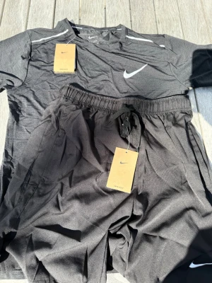 Nike Miler Träningsset – Svart (storlek M) - Stilrent och klassiskt svart Nike Miler-set med t-shirt och matchande shorts. Storlek M. Helt nytt och oanvänt med alla taggar kvar (NWT). Tillverkat i Dri-FIT-funktionsmaterial med snygg Nike-logga. Skickas snabbt 🚚💨 ✨ Ett absolut måste i träningsgarderoben. 📩 Skicka gärna ett meddelande vid frågor eller prisförslag! 🛍️ Bundle-rabatt upp till 20%! 📦 Skickas samma eller nästa dag. 
