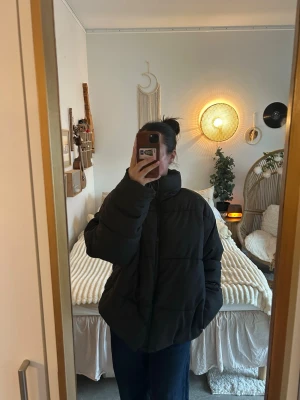 Helt ny Svart oversized pufferjacka - Säljer en svart, oversized pufferjacka med hög krage och breda kanaler. Jackan har en boxig passform och är perfekt för kalla dagar. Stängs med dragkedja framtill och har två sidofickor. Materialet ser ut att vara syntetiskt och jackan är riktigt fluffig.