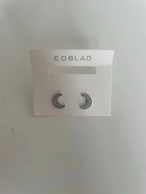 Örhängen från Edblad - Ett par små silvriga halvmåneformade örhängen med gnistrande stenar från Edblad. Aldrig använda! Tveka inte att höra av er om frågor eller prisförslag! 