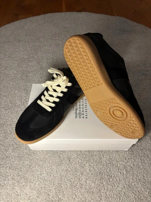 Svarta sneakers med beige sula - Snygga svarta sneakers med beige gummisula och vita snören. Ovandelen är i en mix av mocka och slätt läder för en clean look. Klassisk siluett som passar till det mesta och ger en stilren vibe.