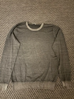 Grå stickad tröja från J.Lindeberg - Snygg grå stickad tröja från J.Lindeberg med rund halsringning och ribbade muddar vid ärmslut och nederkant. Perfekt basplagg i garderoben, enkel att matcha och skön att bära. Materialet känns mjukt och följsamt.