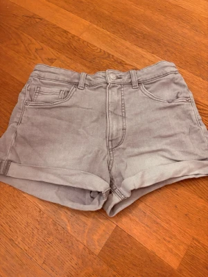 Grå shorts - Snygga grå denimshorts med uppvikta benslut och klassisk femficksdesign. Shortsen har knapp och dragkedja framtill samt bakfickor med lock och knapp. Perfekta för varma dagar och enkel att matcha med olika stilar.