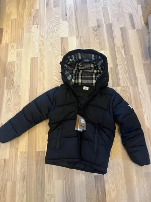 Burberry jacka  - Tja! Nu säljer vi denna sjukt snygga jackan från burberry. Den har det klassiska mönstret i luvan och är väldigt skönt. Den har avtagbara armar som gör den perfekt du när vädret börjar bli kallare. Hör gärna av er vid minsta lilla fråga så får ni ha en trevlig dag! Jag kommer skicka varan 24h efter ni har köpt